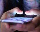 Duas mãos seguram um smartphone com a tela iluminada na penumbra