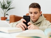 Adolescente vestindo um moletom com capuz digitando em um smartphone, com livros escolares abertos à sua frente