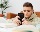 Adolescente vestindo um moletom com capuz digitando em um smartphone, com livros escolares abertos à sua frente