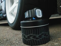 Relógio Casio G-Shock DW5600TT25-1 x Toyo Tires exibido em uma lata de metal com tema de pneu ao lado de uma roda de carro.