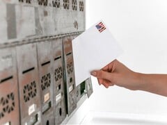 Uma mão colocando um envelope em uma fileira de caixas de correio