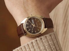 Timex Q 1978 Day and Date com mostrador fumé castanho e caixa em tom dourado, apresentado num pulso com uma bracelete de couro castanho.