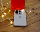 Um OnePlus 15 está sobre uma mesa de madeira, rodeado por luzes de corda que criam um ambiente aconchegante, com uma caixa de varejo da OnePlus em vermelho vivo posicionada ao fundo.