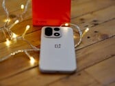 Um OnePlus 15 está sobre uma mesa de madeira, rodeado por luzes de corda que criam um ambiente aconchegante, com uma caixa de varejo da OnePlus em vermelho vivo posicionada ao fundo.