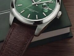 Close-up do relógio Timex Legacy Day and Date, mostrando seu mostrador verde com acabamento raios de sol, aro em tom prateado e asas escovadas, coroa estriada e pulseira de couro marrom texturizado, diante de uma caixa verde-escura e sobre uma superfície de madeira.