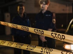 Dois policiais de pé à noite atrás de uma fita amarela onde se lê Pare