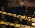 Dois policiais de pé à noite atrás de uma fita amarela onde se lê Pare