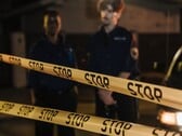 Dois policiais de pé à noite atrás de uma fita amarela onde se lê Pare