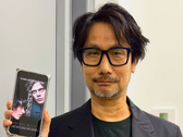 Hideo Kojima mostrando um pôster de Physint em seu celular