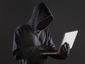 Um hacker encapuzado operando um laptop em um fundo escuro.