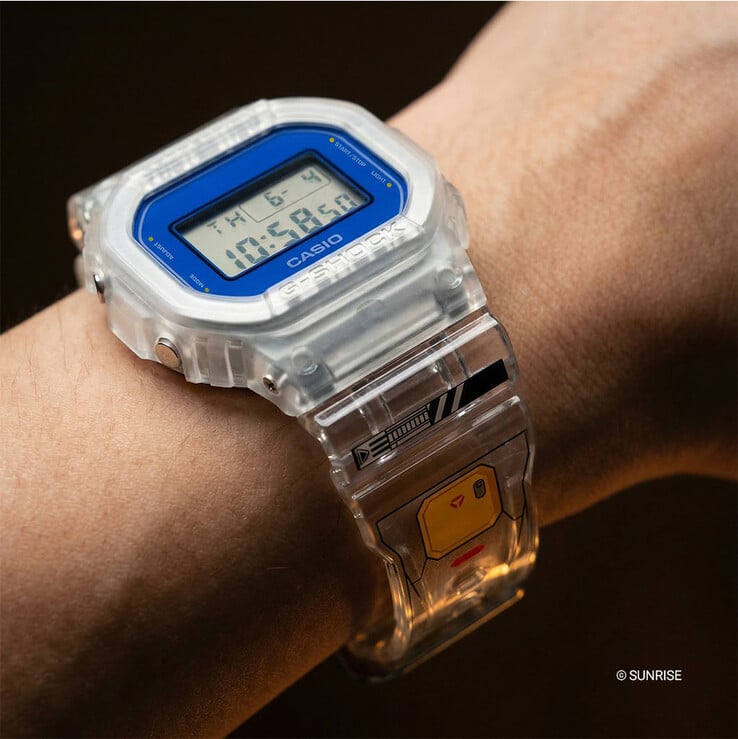 Casio G-Shock x Mobile Suit Gundam DW-5600GM26-7DR usado no pulso, com caixa e pulseira de resina transparente, moldura azul e gráficos inspirados em Gundam na pulseira.