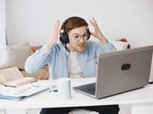 Homem usando fones de ouvido levantando as mãos em sinal de frustração diante de um laptop