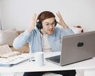 Homem usando fones de ouvido levantando as mãos em sinal de frustração diante de um laptop
