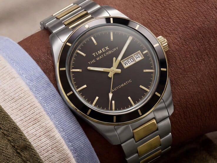 Relógio Timex Waterbury Heritage Automatic bicolor, com mostrador preto, usado no pulso, exibindo o indicador de dia e data e detalhes em tom dourado.
