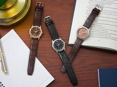 Três relógios Citizen Rolan dispostos sobre uma mesa de madeira ao lado de um caderno, uma caneta, um abajur e um livro aberto, incluindo o modelo AW2110-14Z com mostrador cor de salmão.