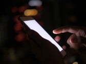 Mão segurando um smartphone com a tela brilhando no escuro