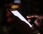 Mão segurando um smartphone com a tela brilhando no escuro