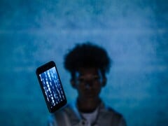Smartphone flutuante com código no ecrã em frente a um fundo azul, com uma pessoa desfocada atrás dele