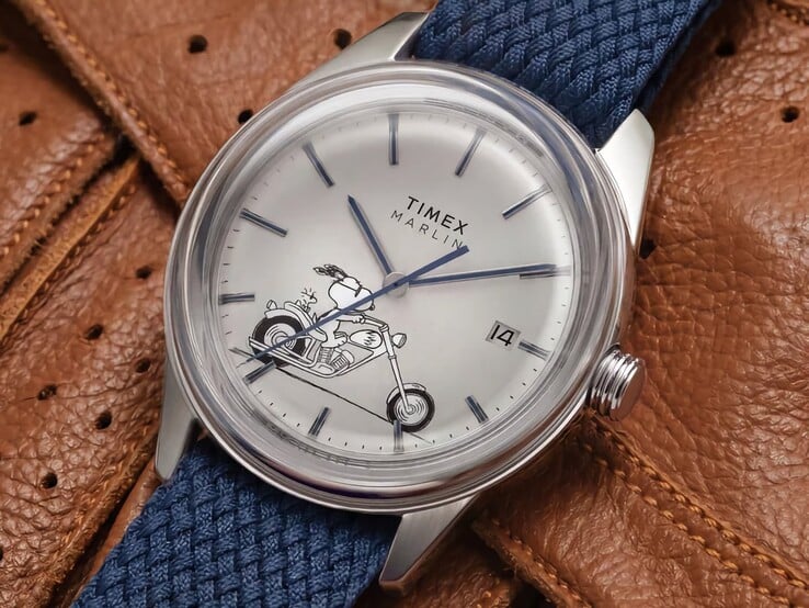 Vista frontal em ângulo do relógio Peanuts x Timex Marlin Jet Automatic Easy Rider, destacando o cristal abaulado, a caixa em aço inoxidável com acabamento prateado, o mostrador com tema do Snoopy e a pulseira de tecido azul.