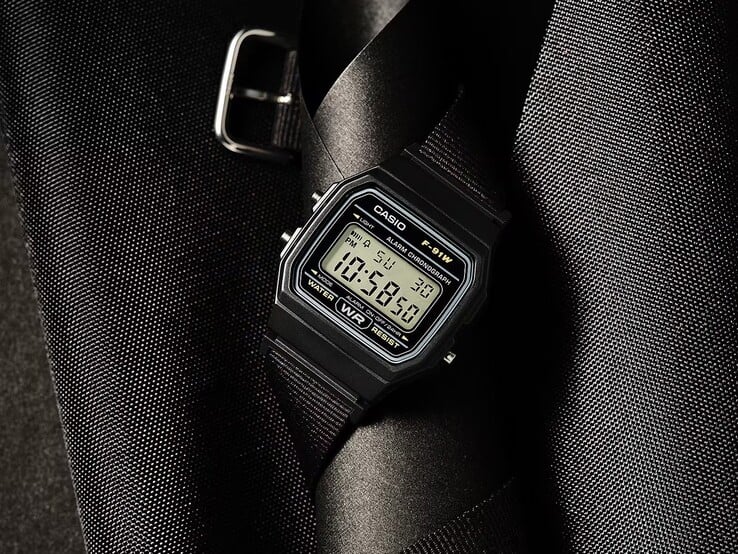 Relógio digital Casio F-91WF-1A com caixa preta, pulseira de tecido preto trançado e detalhes prateados, fotografado contra um fundo escuro texturizado.