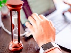 Uma ampulheta ao lado de uma mão sobre o teclado de um laptop