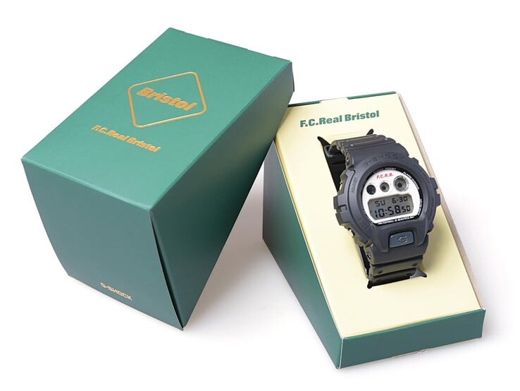 O Casio G-Shock x F.C. Real Bristol DW-6900 está exposto dentro de uma caixa de apresentação verde com a marca conjunta, com a capa externa combinando ao lado.