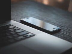 Um smartphone ao lado de um laptop aberto sobre uma mesa escura