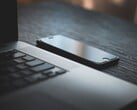 Um smartphone ao lado de um laptop aberto sobre uma mesa escura