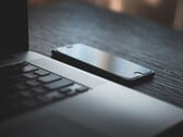 Um smartphone ao lado de um laptop aberto sobre uma mesa escura