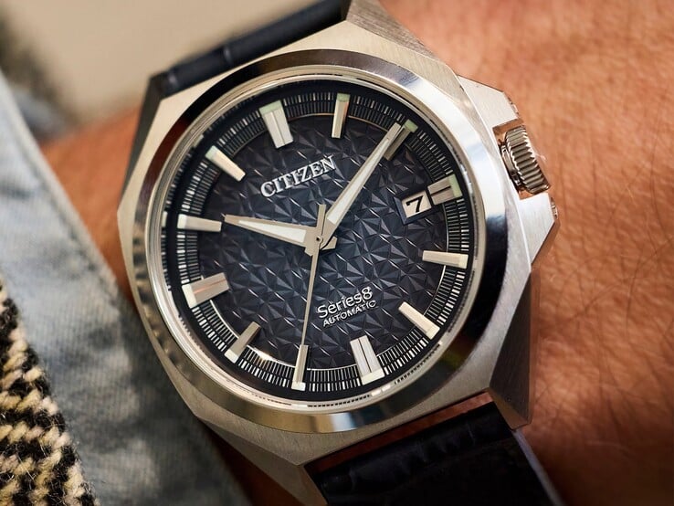 Relógio automático Citizen Série 8 831 com mostrador geométrico nas cores laranja-queimado e marrom, caixa e luneta douradas e pulseira integrada com elos em H dourados, usado no pulso.