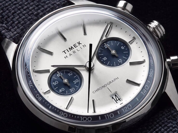Close-up do cronógrafo Timex Marlin Jet TW2Y89900, mostrando seu mostrador branco-prateado, submostradores azul-marinho, marcadores de hora aplicados, ponteiros tipo bastão, escala taquimétrica e janela de data.