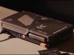 Um console de videogame compacto feito sob medida, equipado com um mini PC, aberturas de ventilação expostas, portas USB e botões de ligar na cor laranja sobre uma mesa.