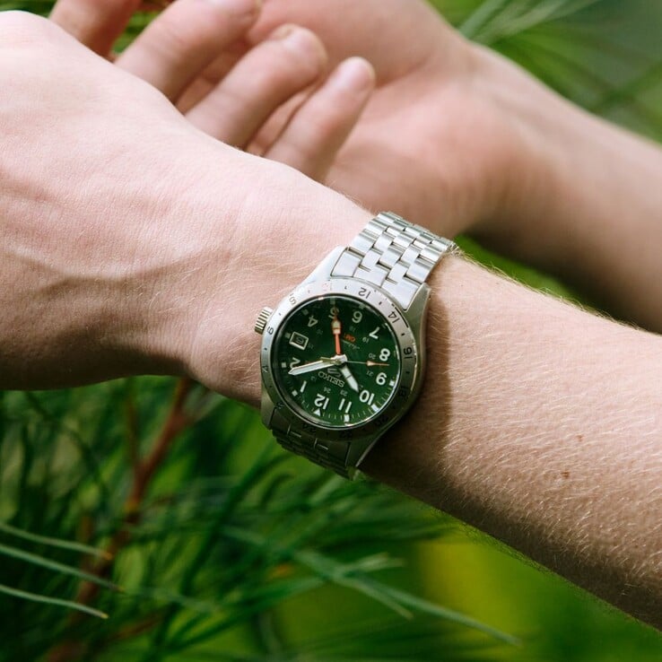 Vista frontal do Seiko 5 Sports Field GMT HDB001, com mostrador verde, luneta fixa de 24 horas em aço inoxidável, ponteiro GMT laranja e pulseira de aço com cinco elos.