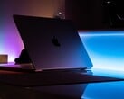 Um MacBook entreaberto em uma sala escura, com a luz se espalhando pela fresta sobre a mesa