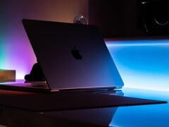 Um MacBook entreaberto em uma sala escura, com a luz se espalhando pela fresta sobre a mesa