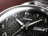 Grande plano do mostrador preto do Casio MTP-E735AR, com um intrincado padrão de arabescos, algarismos árabes orientais em relevo, ponteiros polidos em tom prateado e uma janela de dia e data às 3 horas.