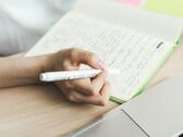 Uma pessoa está escrevendo anotações em um caderno ao lado de um laptop aberto