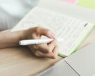 Uma pessoa está escrevendo anotações em um caderno ao lado de um laptop aberto
