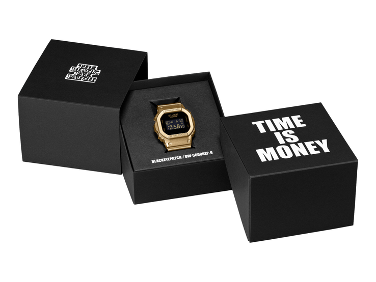 Um relógio Casio G-Shock DW-5600BEP-9 dourado, com display digital preto, está posicionado entre duas caixas de apresentação pretas. O relógio exibe a marca BlackEyePatch no mostrador, enquanto a caixa em primeiro plano traz a inscrição “TIME IS MONEY”.