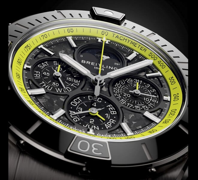 Grande plano do Breitling Super Chronomat B19 44 Perpetual Calendar Chronograph, mostrando o seu mostrador em fibra de carbono, submostradores do calendário, ponteiros em tom prateado e escala taquimétrica verde-lima.