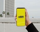 Uma mão segurando um smartphone com a palavra “eSIM” em letras grandes em uma tela amarela.