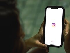 Mulher segurando um smartphone com as duas mãos; a tela exibe a página inicial do Instagram