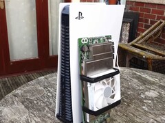 Um console PlayStation 5 colocado ao lado de uma placa AMD BC250 personalizada montada com um dissipador de calor e um ventilador de resfriamento. (Fonte da imagem: Budget-Builds Official via YouTube)