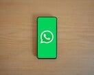 Smartphone sobre uma mesa de madeira, exibindo a tela inicial verde do WhatsApp com seu logotipo.