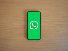 Smartphone sobre uma mesa de madeira, exibindo a tela inicial verde do WhatsApp com seu logotipo.